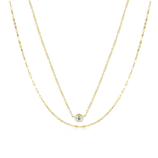 A double strand gold necklace with a bezel set clear stone on the shorter of the two chains on a white background