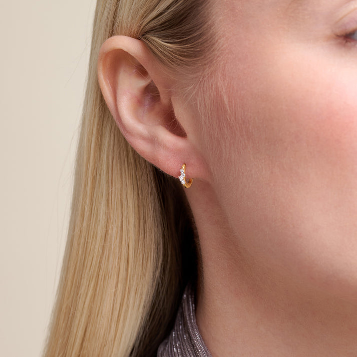 Close-up of a person wearing a gold earring with a beige background
