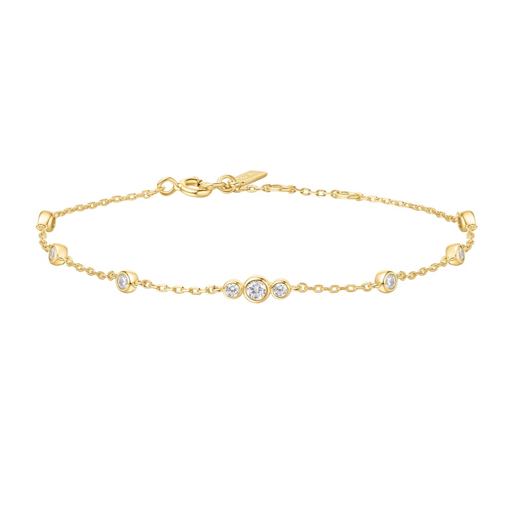 A gold bracelet with stationed bezel set clear, round stones on a white background