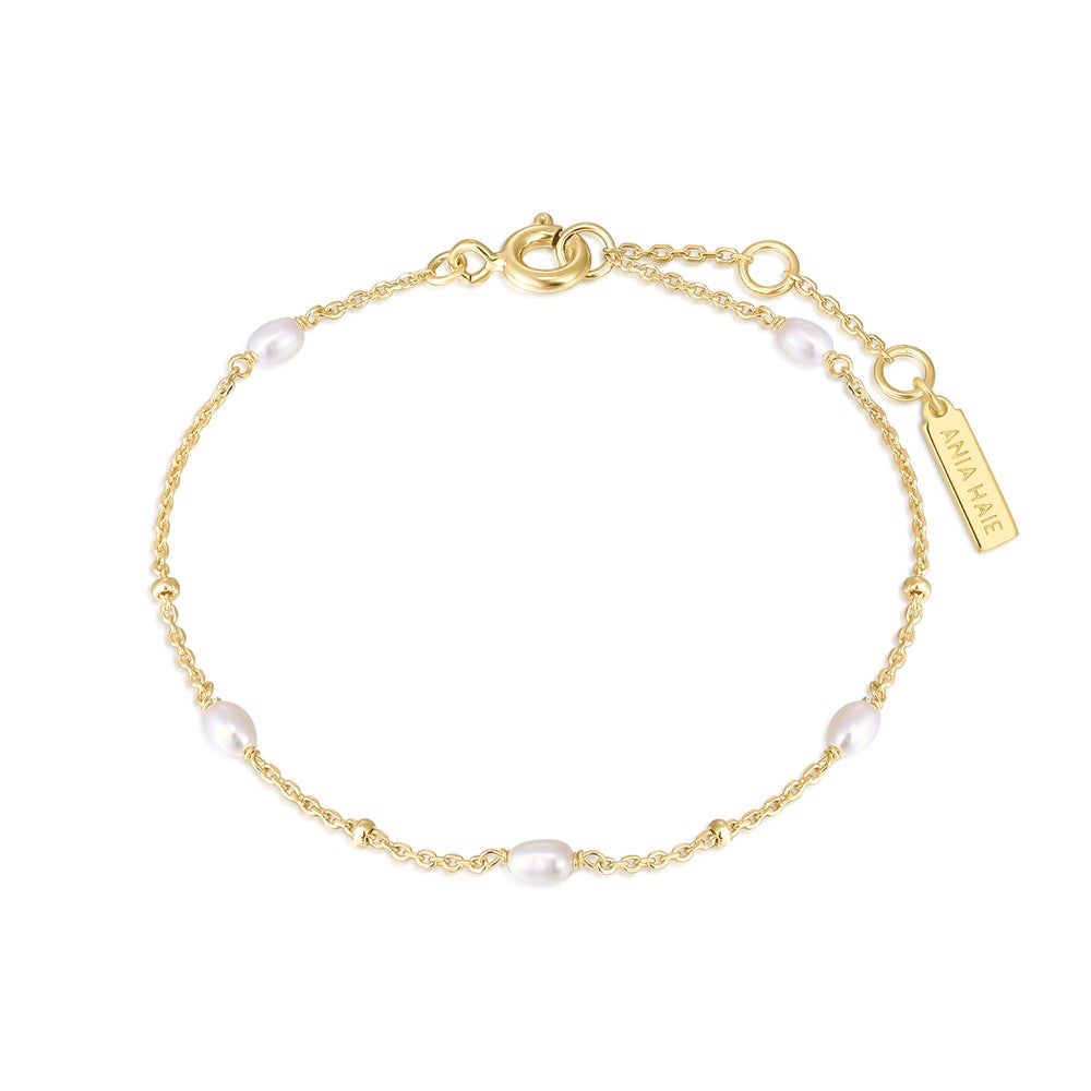 A delicate gold chain bracelet with irregular white freshwater pearls spaced along the chain, featuring a lobster clasp, extender chain, and a small rectangular brand tag on a white background